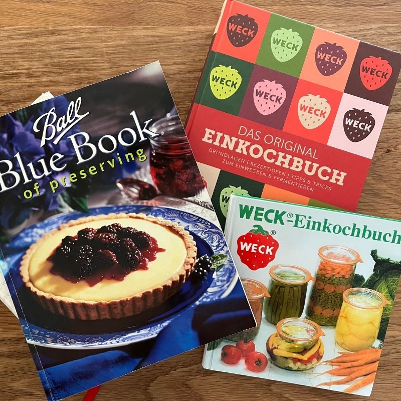 Ball Blue Book and two WECK cookbooks on canning, shown on a wooden surface