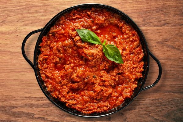 Spaghetti Bolognese sauce in a cast-iron pot sitting on a wooden countertop
