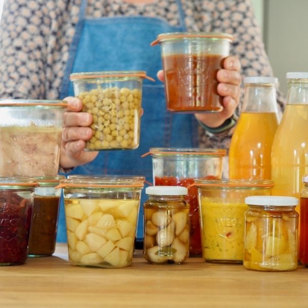 Author holding jars of home canned chickpeas, sauces, and fruits.