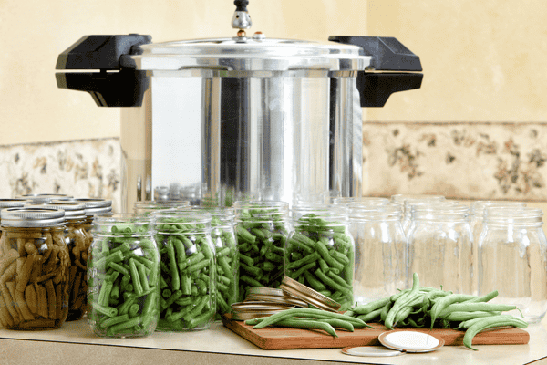 Pressure canner on a kitchen counter surrounded by jars of fresh and canned green beans