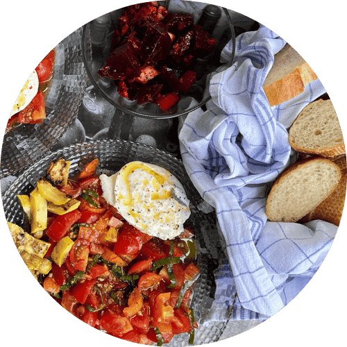 Tray with plates of tomato salad, roasted summer squash, and burrata mozzarella with sliced baguette.