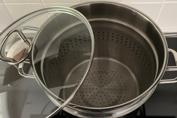 Large noodle pot with steamer insert and lid sitting on a cooktop