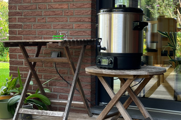 Electric canner sitting on a low wooden table on a covered terrace, with another table next to it.