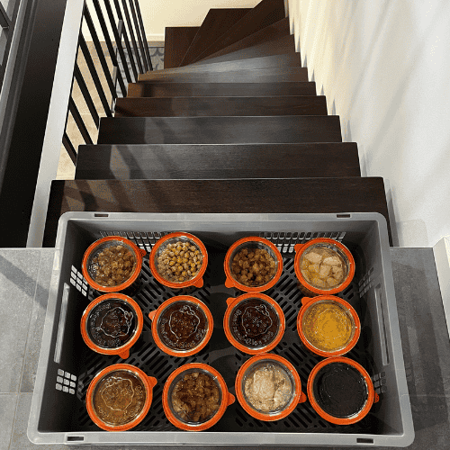 Plastic crate lined with jars of preserved food at the top of a staircase.